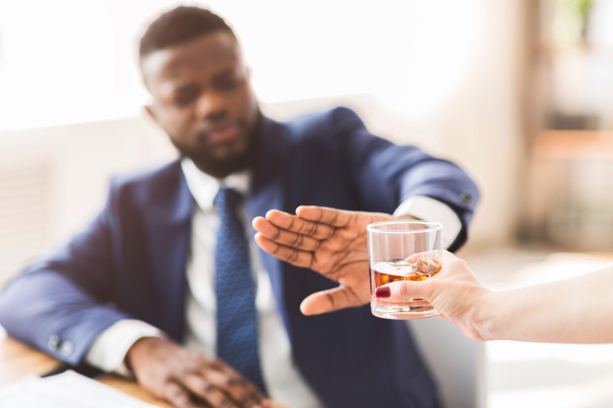 Businessman saying no to glass of whiskey offered by colleague