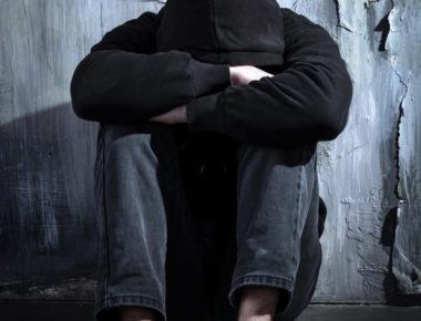 Drug addict wearing a hoodie sitting alone