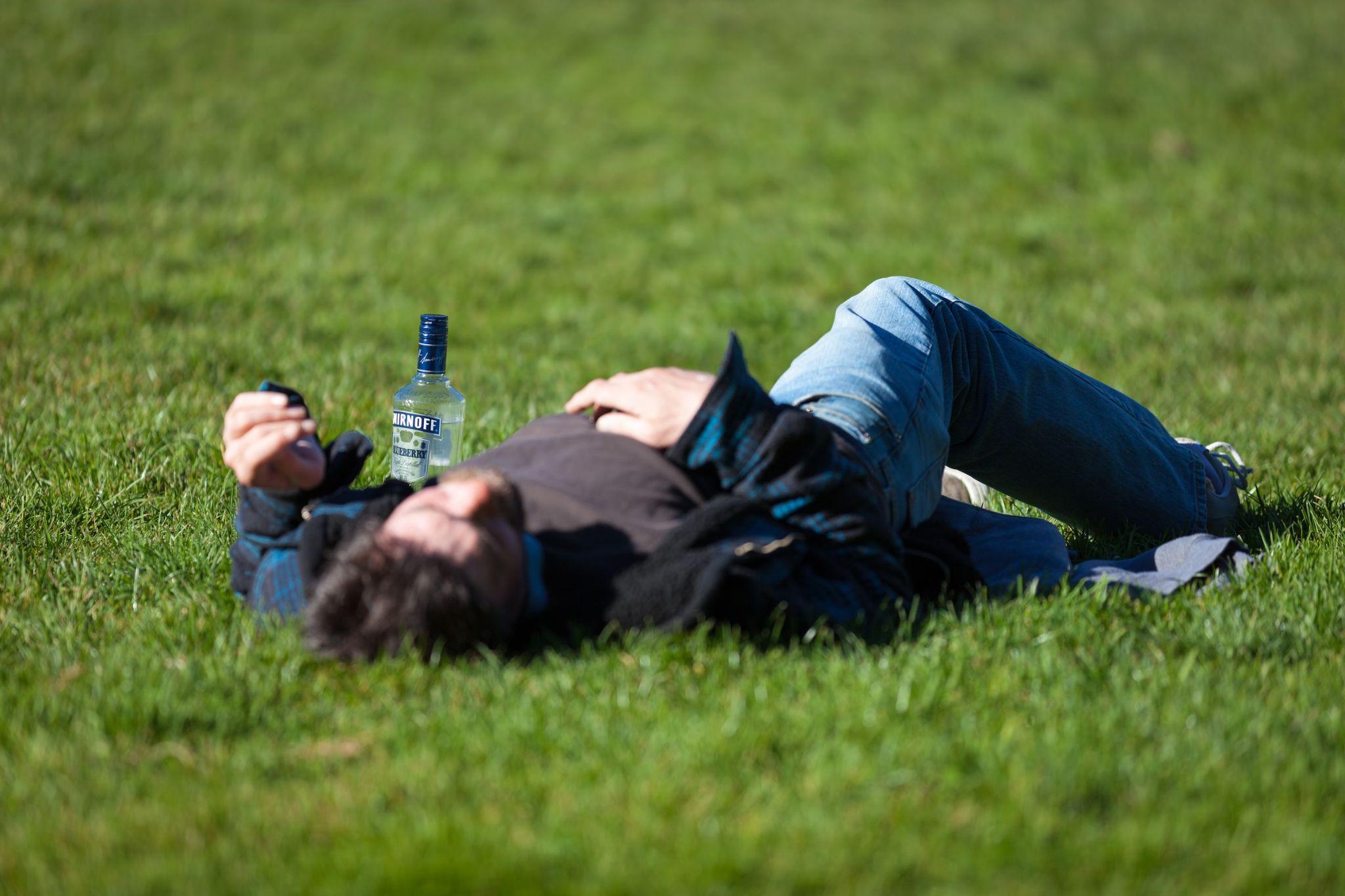 Drunk Man Laying On Grass With Bottle Of Alcohol