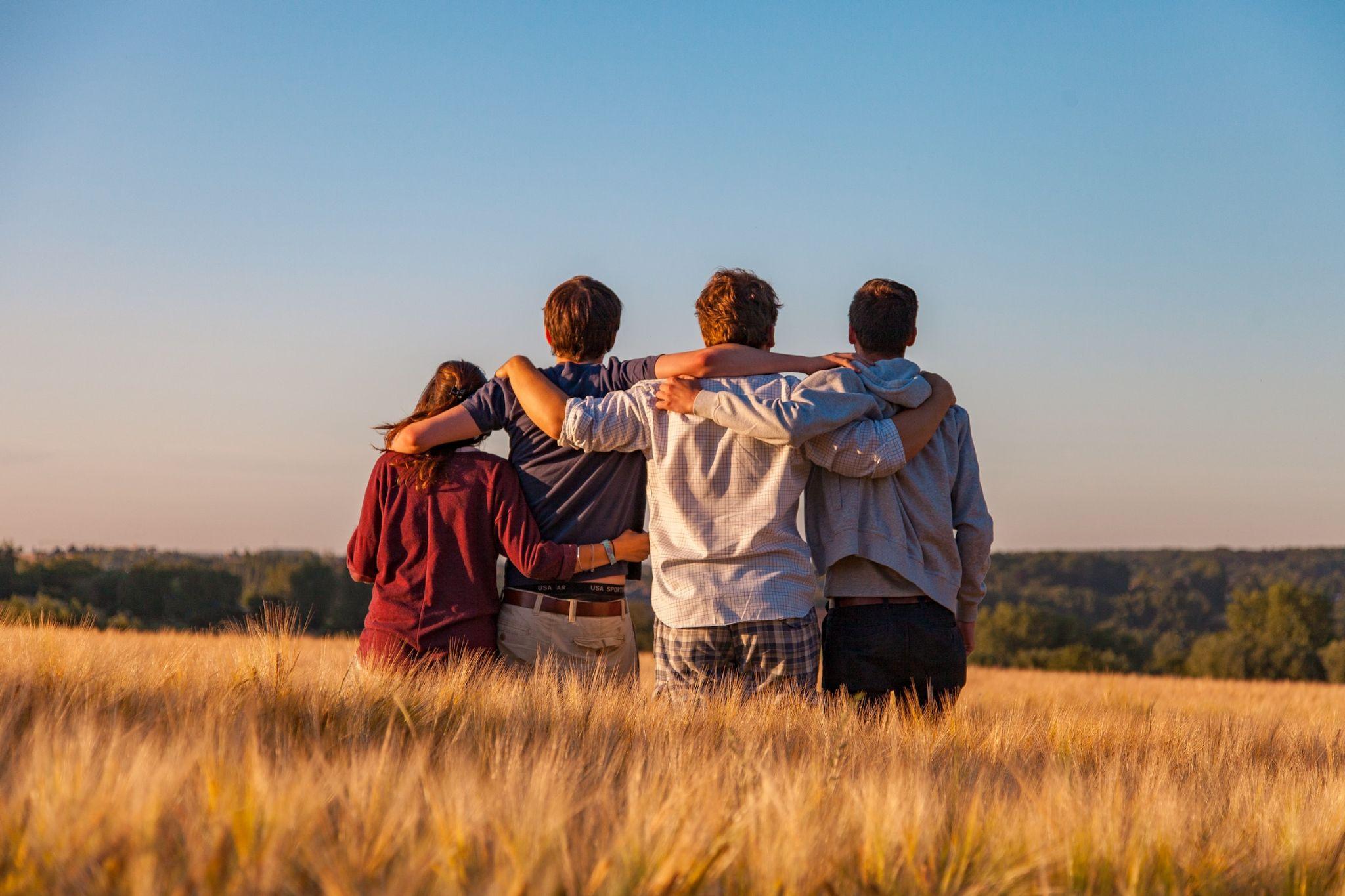 Four Friends Hugging In A Grass Field