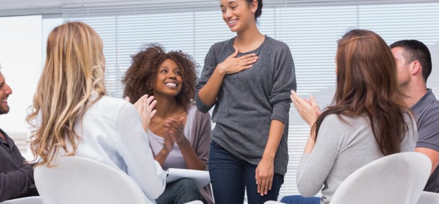 Happy patient has a breakthrough in group therapy while others are clapping her