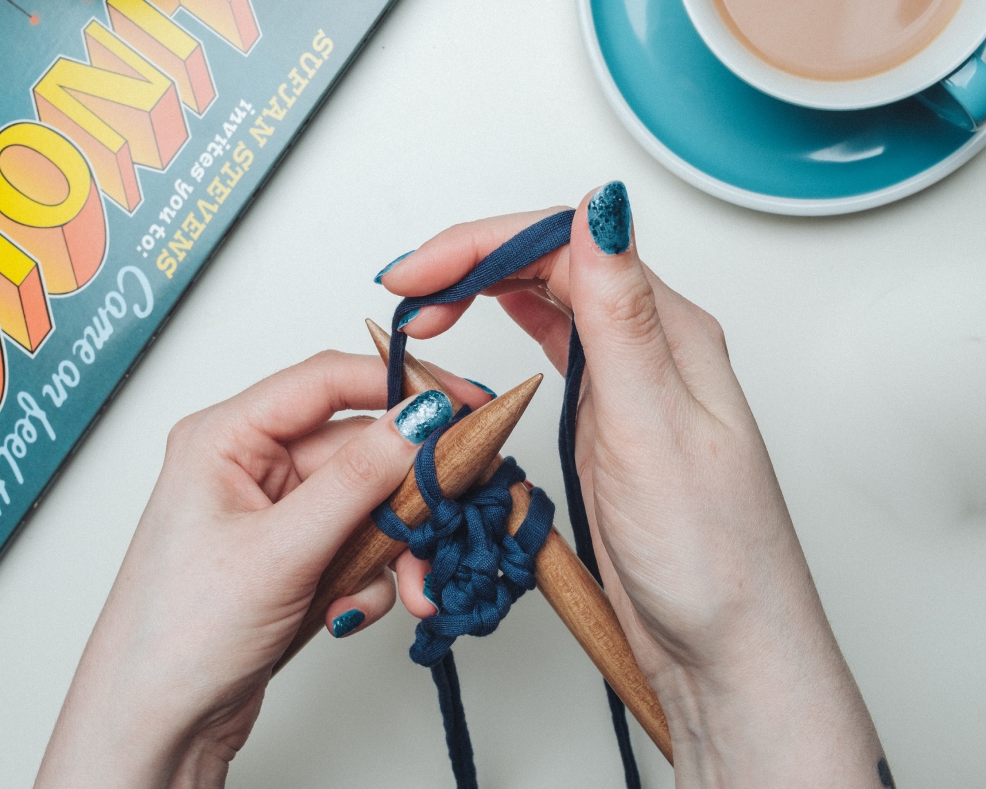 person tying blue lace on two brown sticks beside teal and white ceramic teacup set
