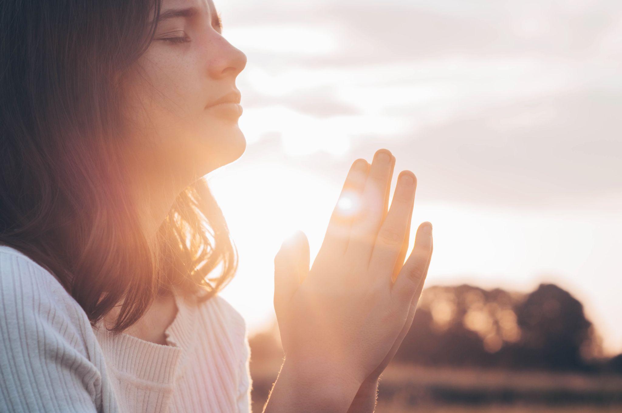 Teenager Girl closed her eyes, praying in a field during beautiful sunset
