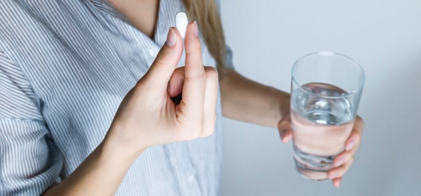 woman holding glass water and white medicine pill