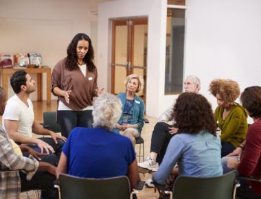 Woman Standing To Address Self Help Therapy Group Meeting In Community Center