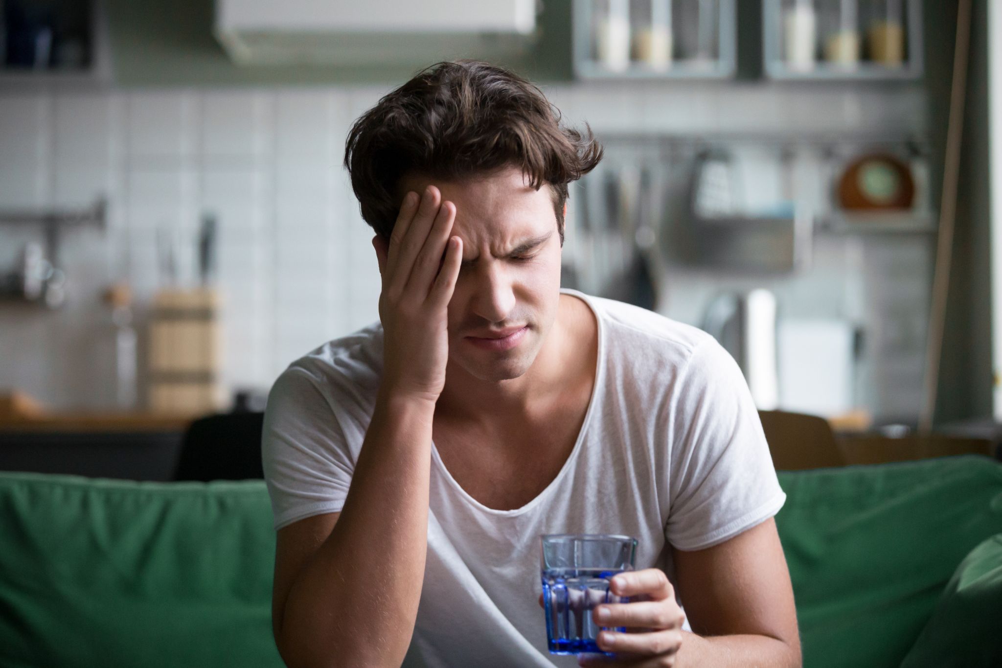 Young man suffering from strong headache sitting with glass of water