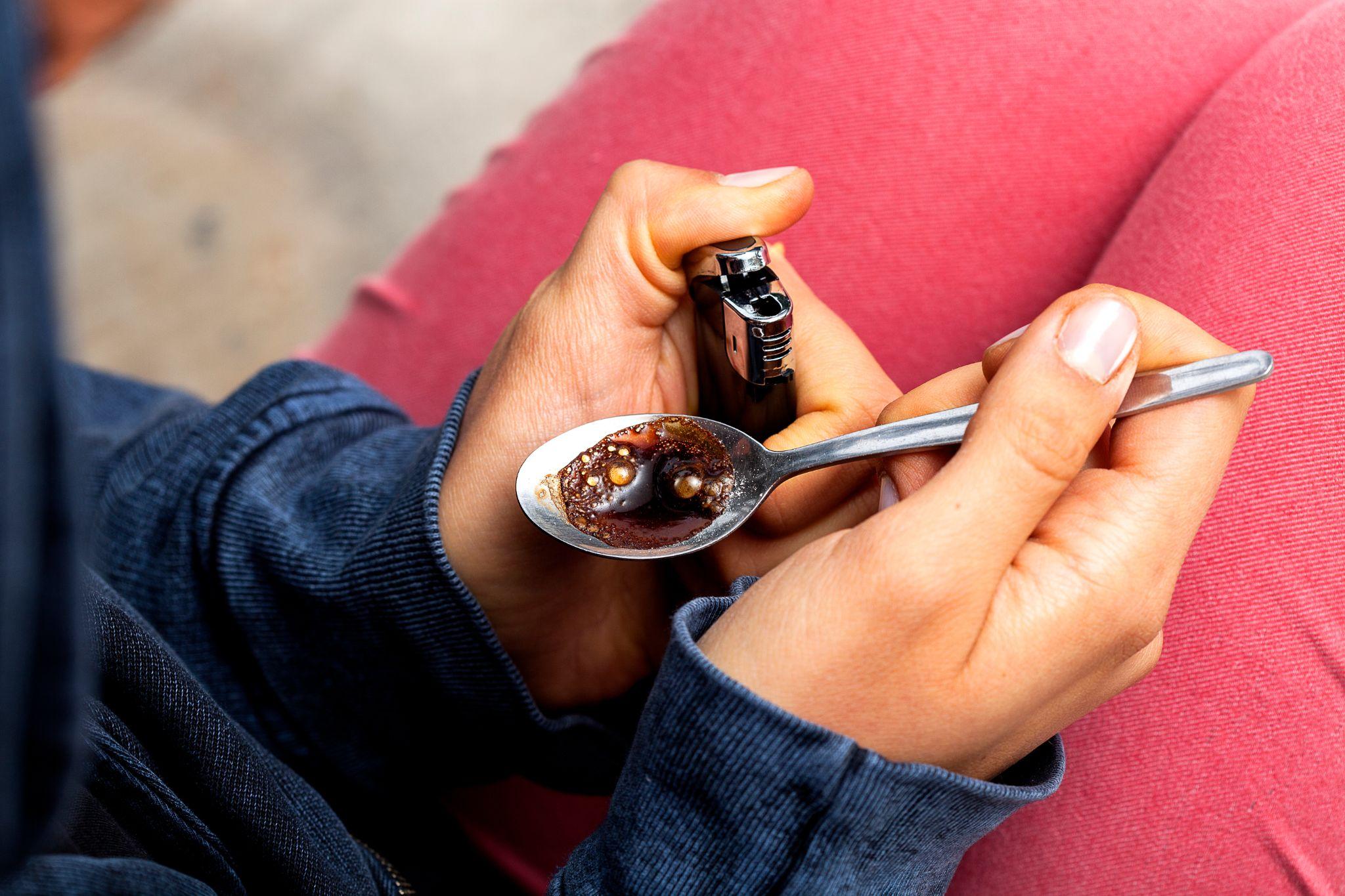Young woman with a lighter and a spoon preparing a dose of heroin